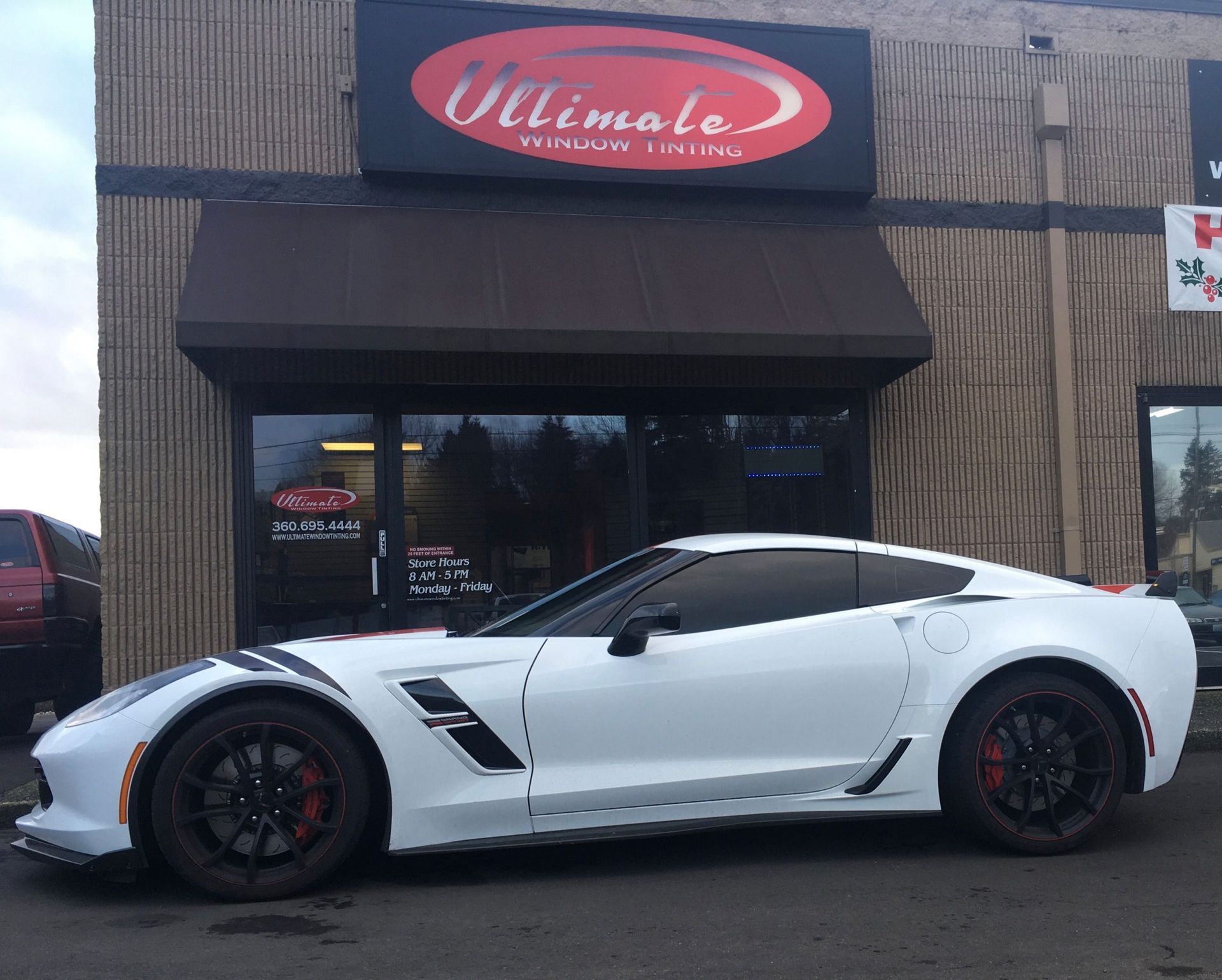 White sports car parked outside an auto shop with a red sign above the entrance
