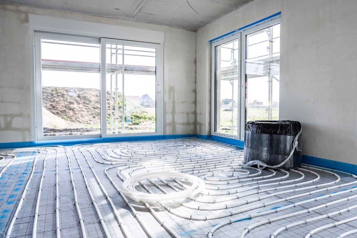 Underfloor heating system installation in a room with windows, exposed piping, and a bucket — Demetrius Projects in Queanbeyan East, NSW