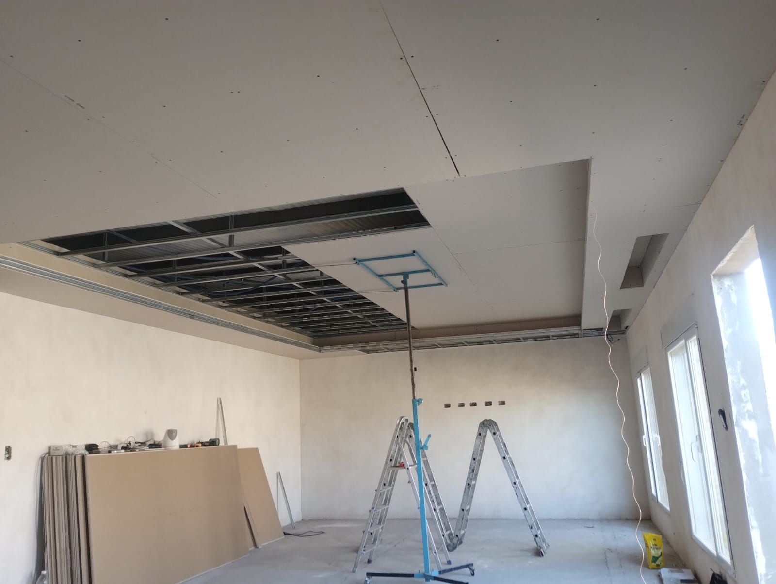Habitación en obras con reparación de techo, escaleras y materiales de construcción bajo un panel de techo abierto.