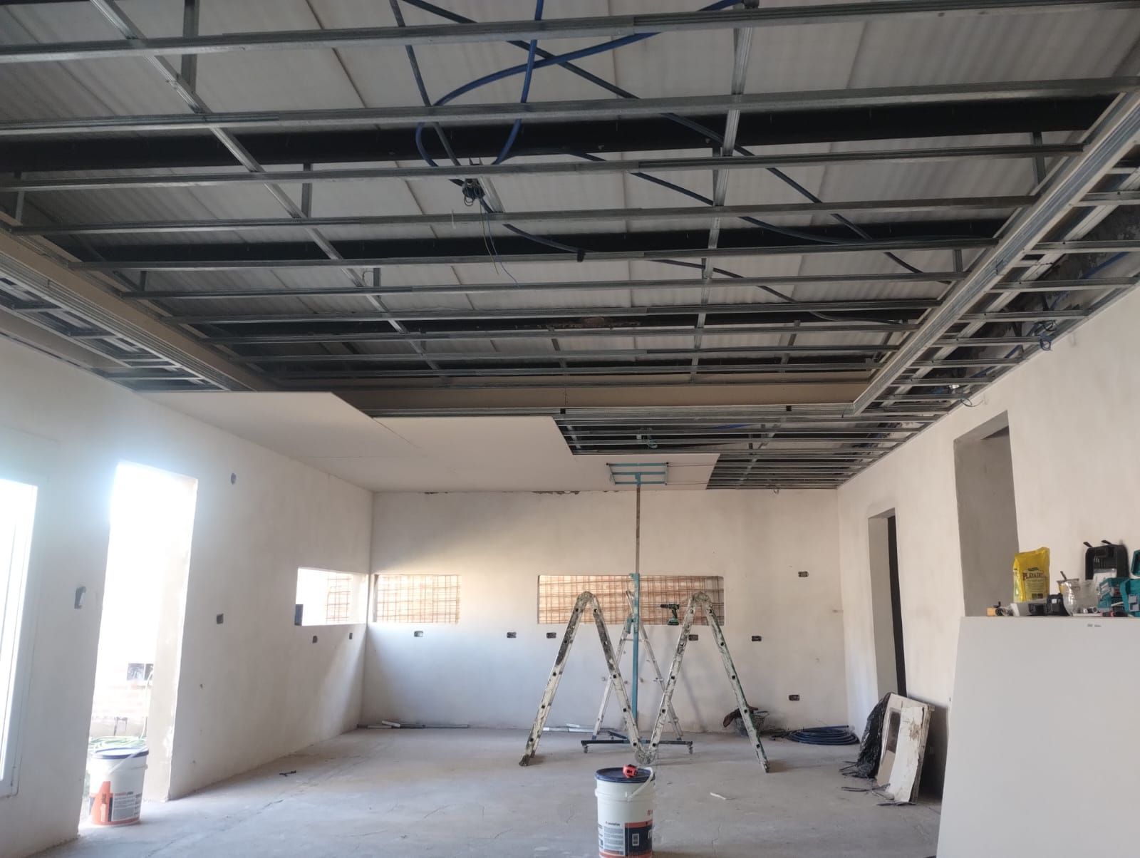 Habitación vacía sin terminar, con vigas de techo a la vista y maquinaria de construcción en el suelo.
