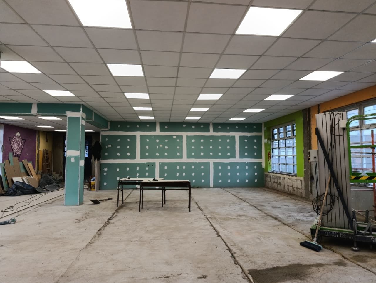 Habitación vacía en obras con paredes verdes, suelo visto y techo a cuadros.