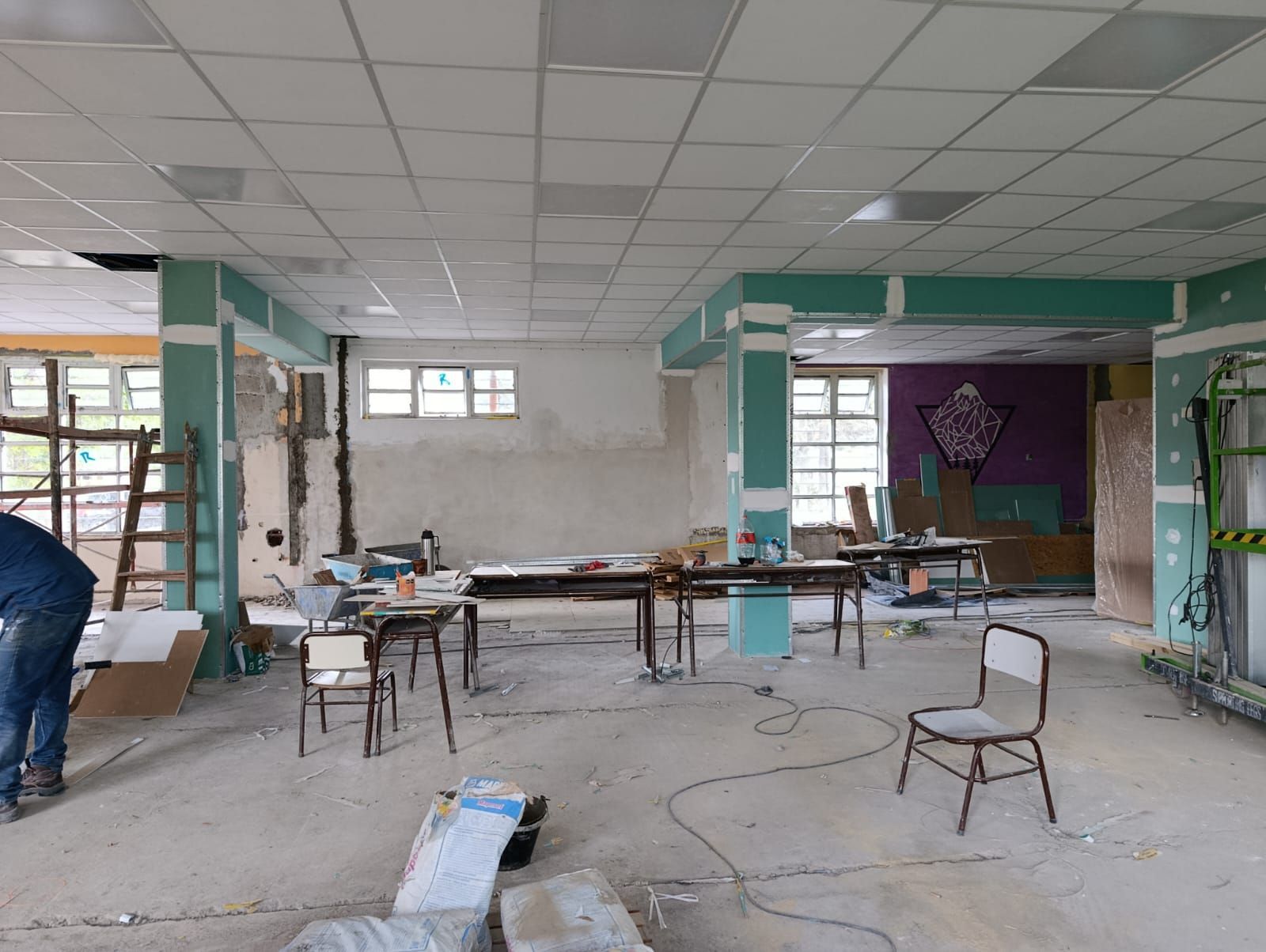 Habitación reformada con herramientas, sillas y cables dispersos, paredes sin terminar y techo falso.