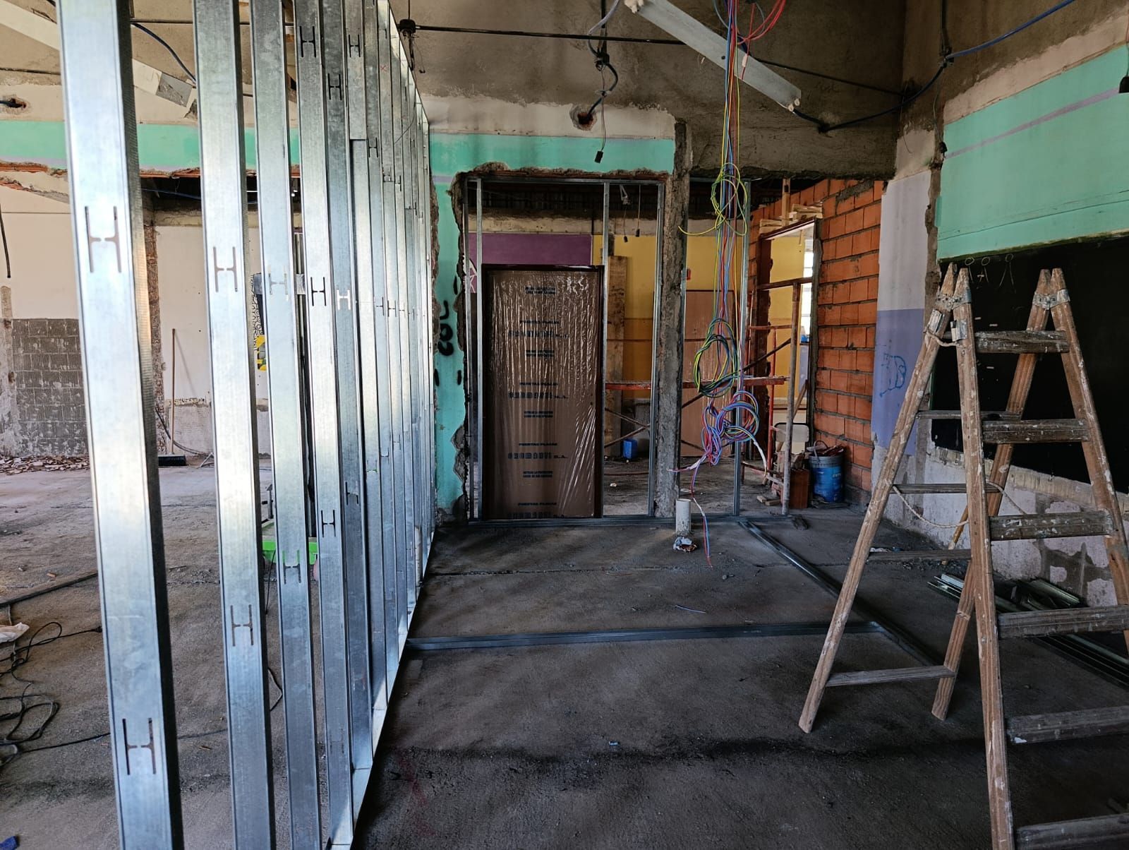 Interior de una casa en renovación con vigas a la vista, una escalera y paredes sin terminar.