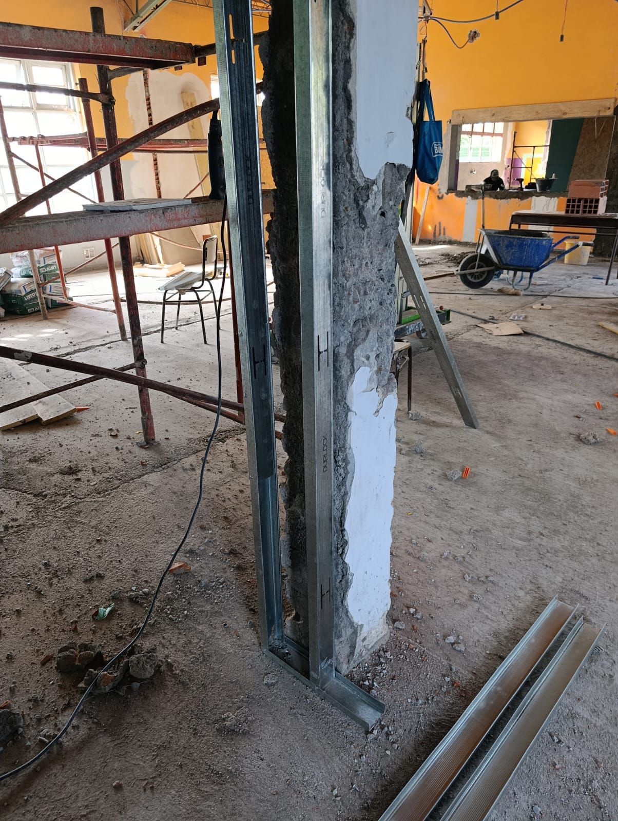 Pilar de hormigón dañado en reparación en una obra, con andamios y herramientas cerca.