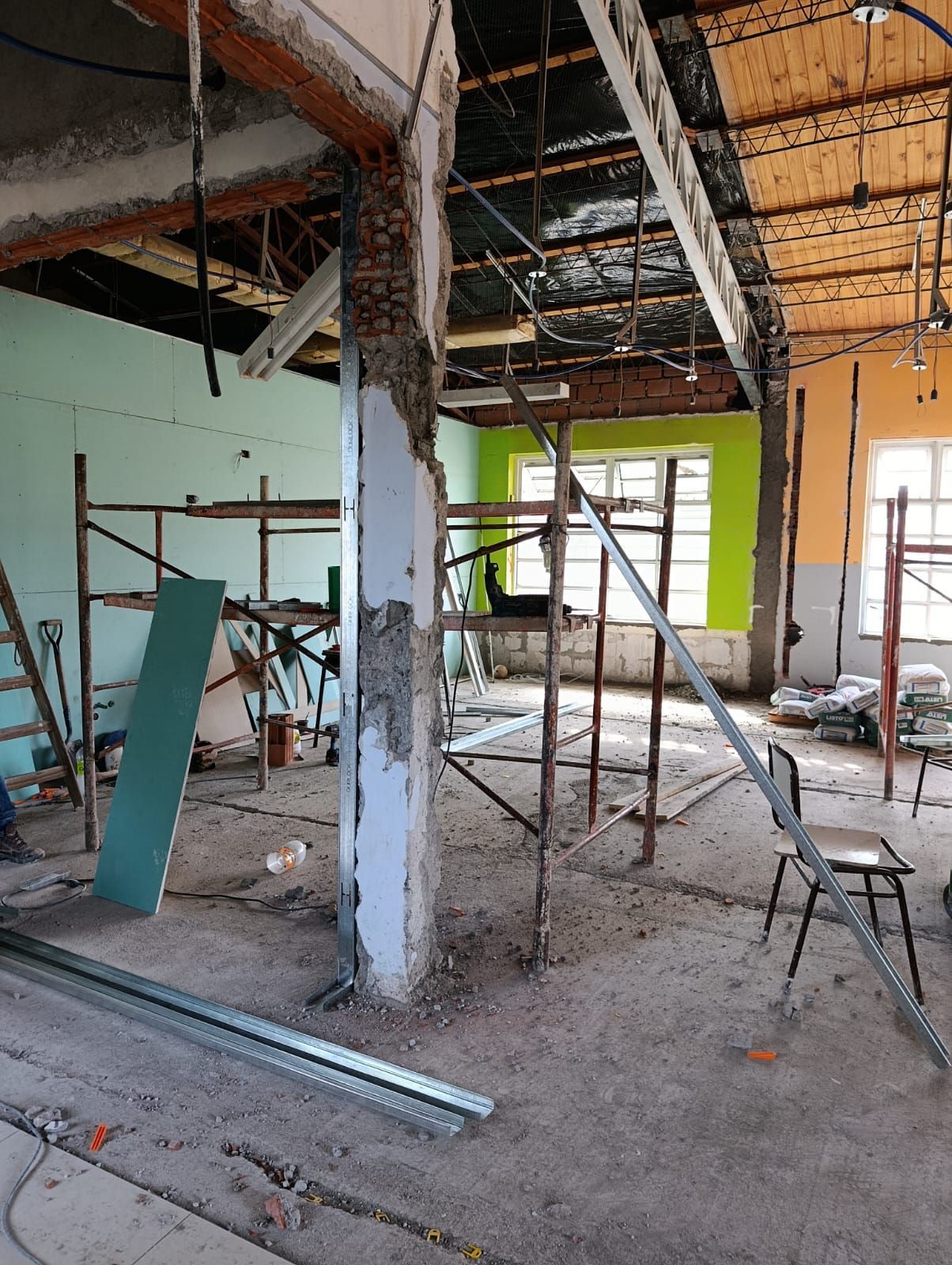 Interior parcialmente demolido con vigas a la vista, andamios, escombros y una pared con ventanas.