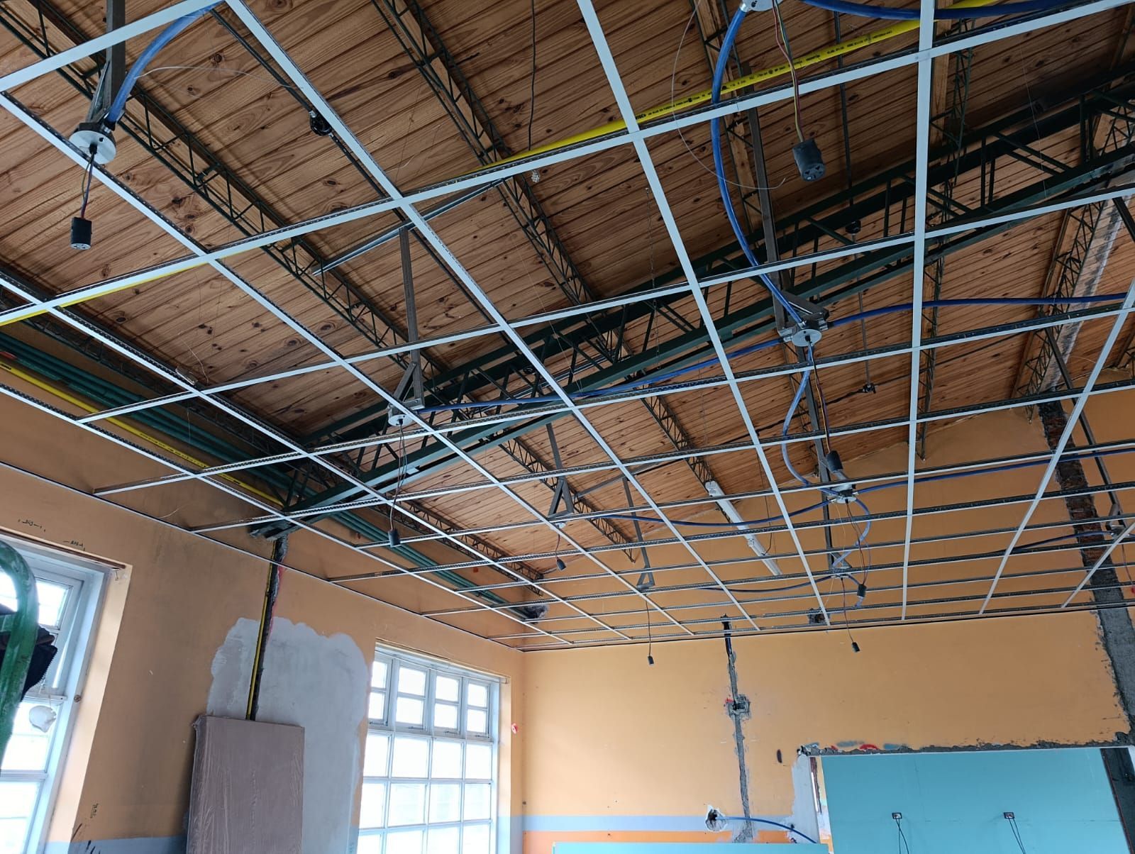 Techo en construcción con estructura metálica y cableado a la vista en una habitación con paredes color beige y una ventana.
