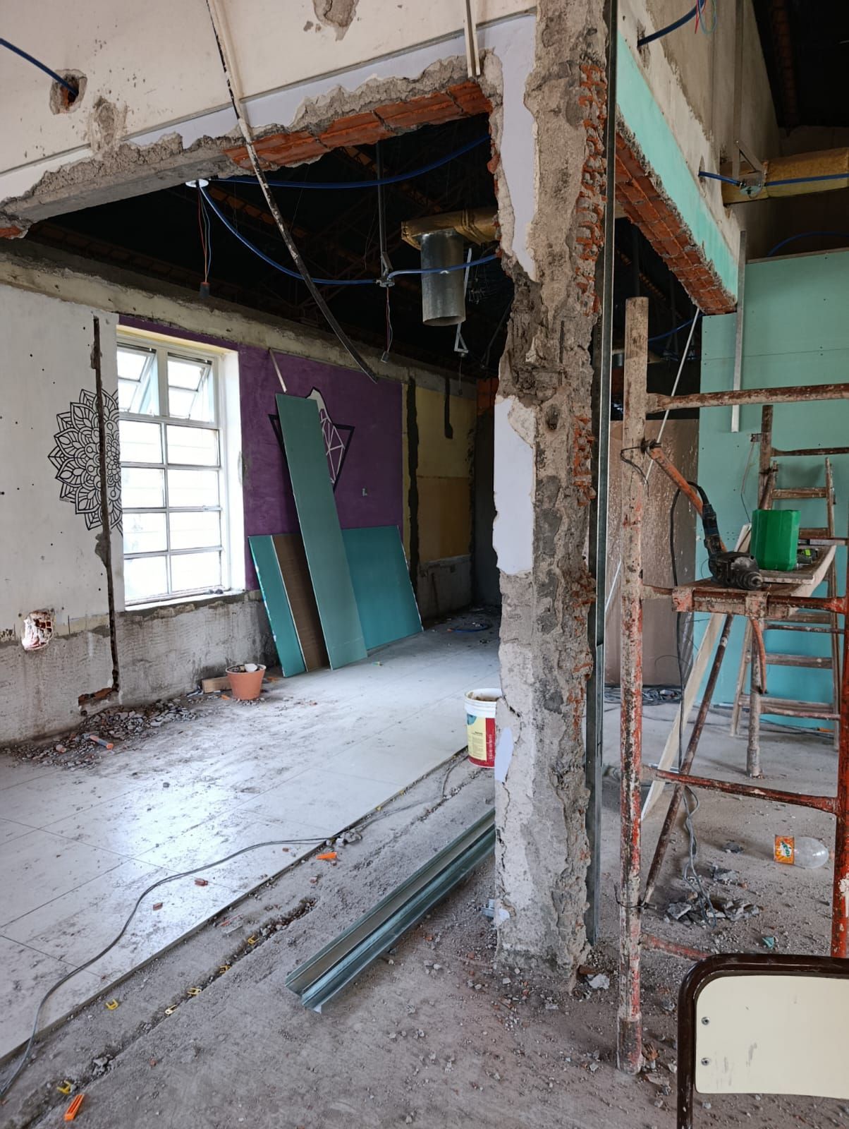 Interior parcialmente demolido con vigas expuestas, escombros y tablones inclinados cerca de una ventana.