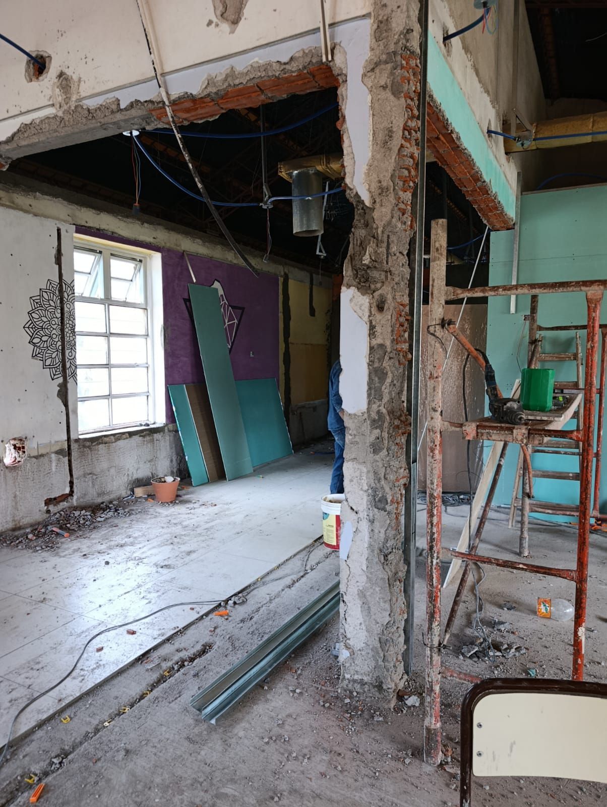 Habitación parcialmente demolida con vigas expuestas, escombros, escaleras y paredes sin terminar en proceso de renovación.