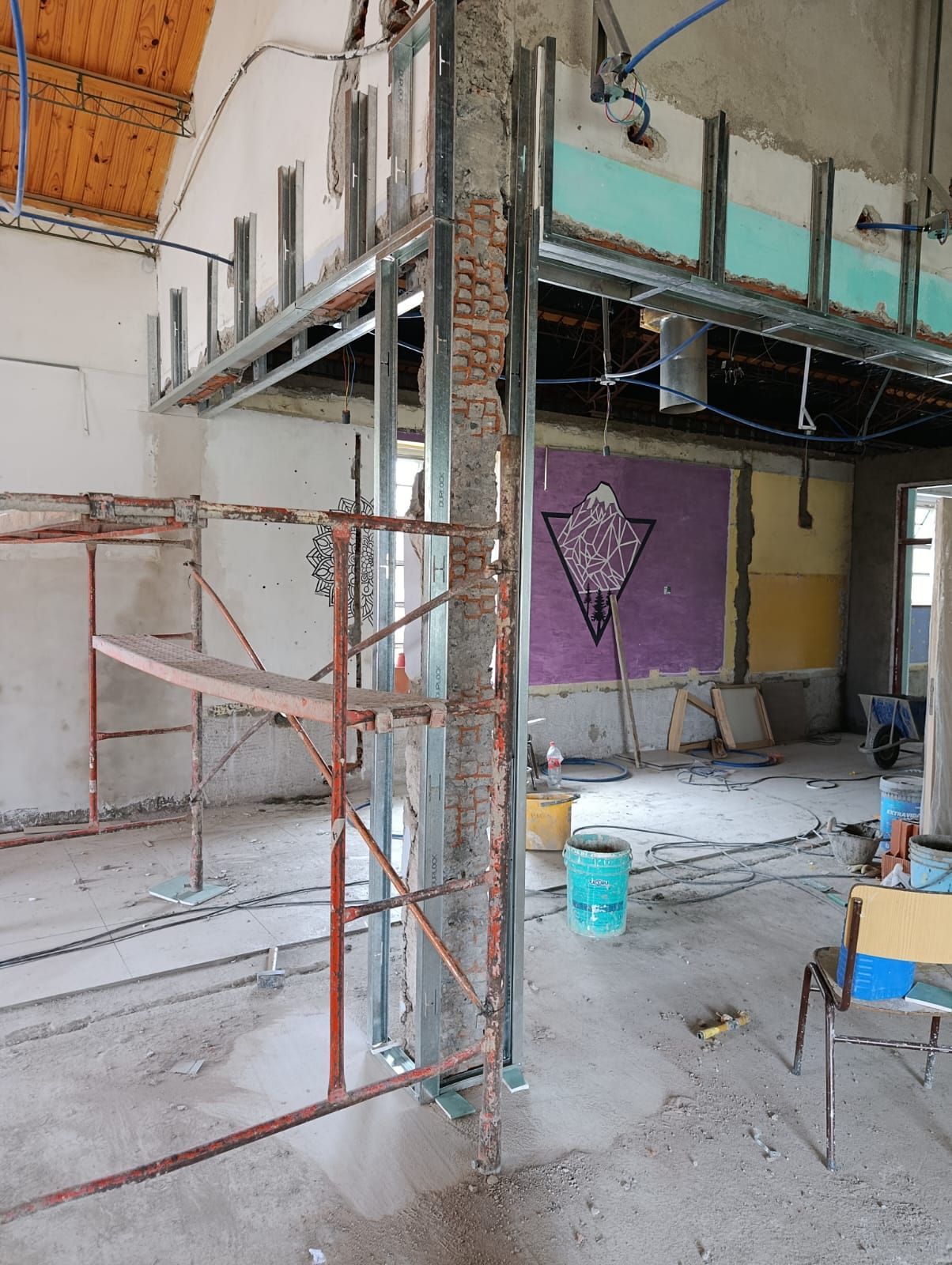 Interior en obras con andamios, paredes sin terminar y materiales de construcción en el suelo.