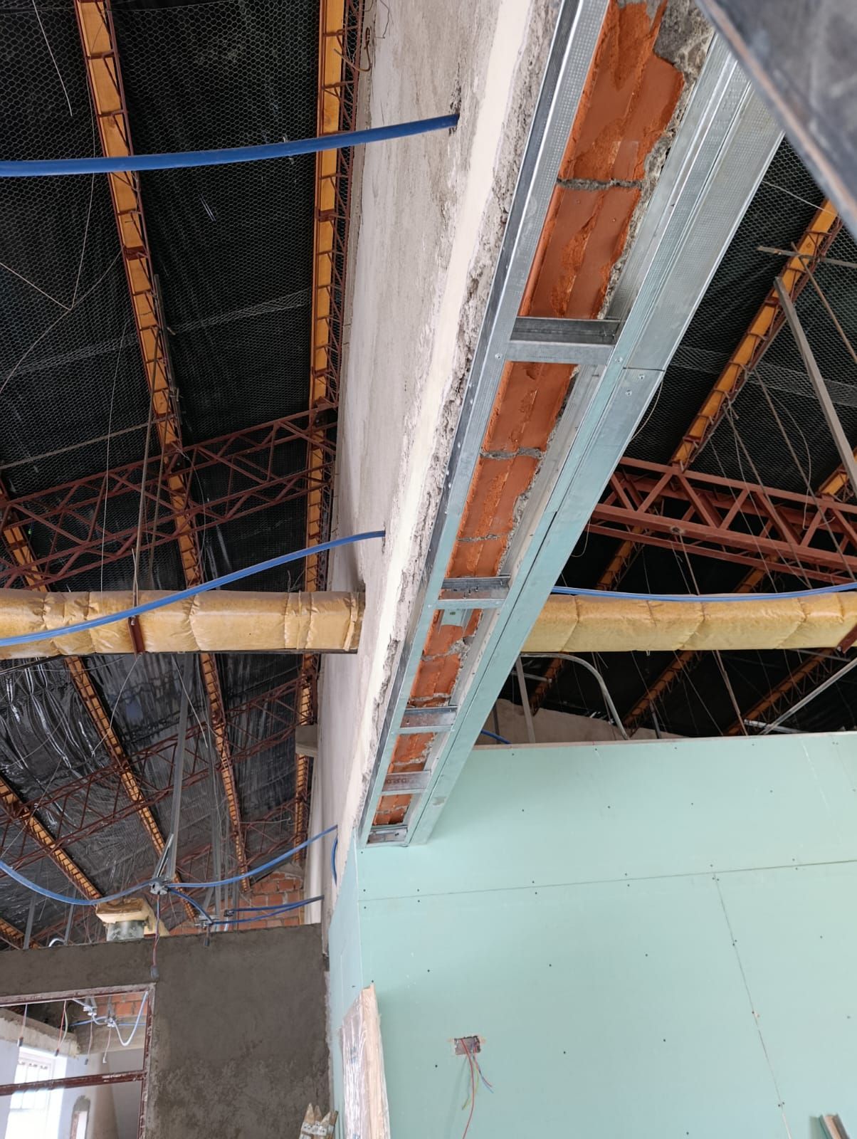 Techo en construcción con vigas a la vista, conductos metálicos y cables colgantes en un interior sin terminar.
