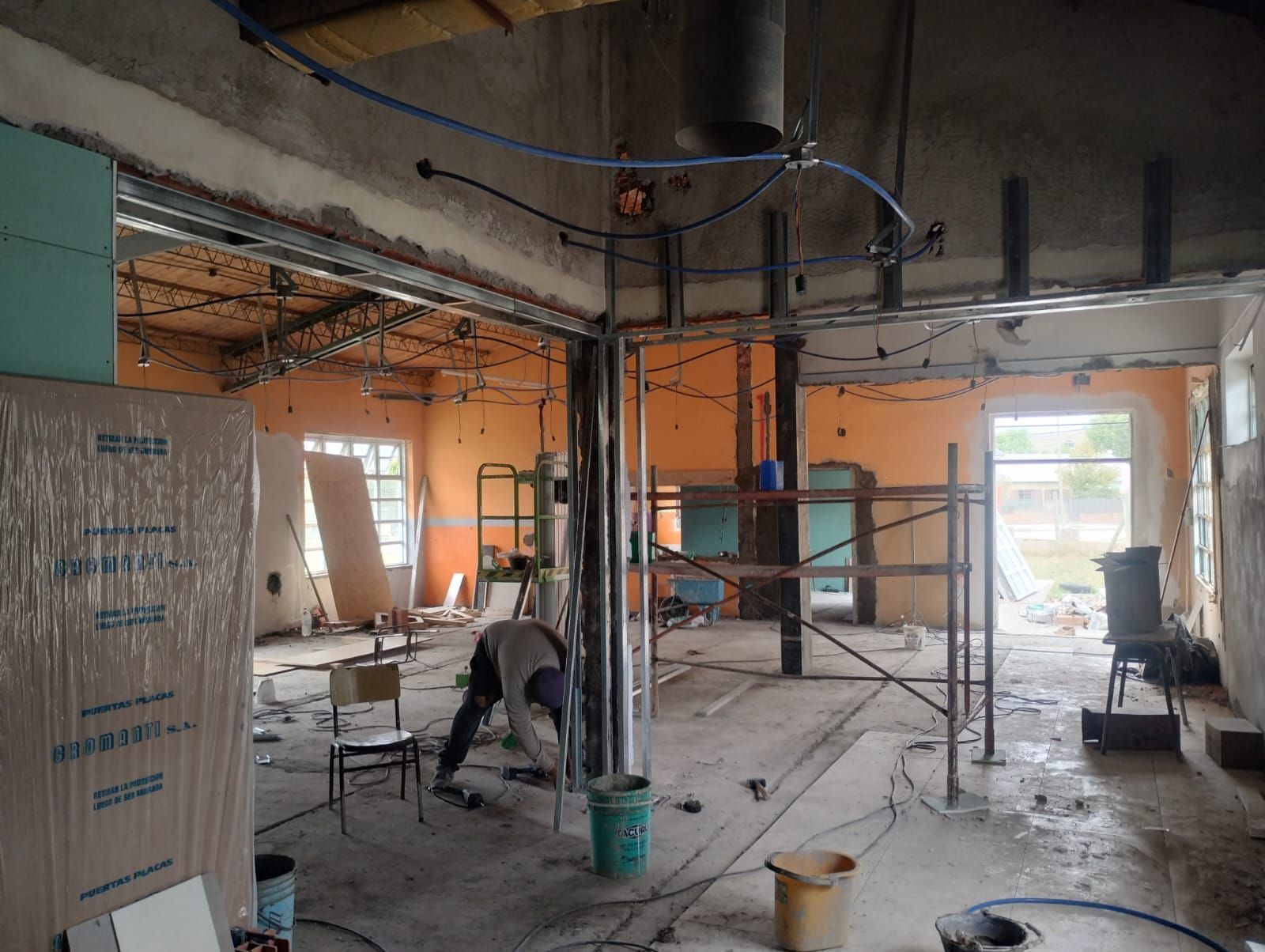 Obra en construcción con andamios, cableado expuesto y trabajadores dentro de una habitación sin terminar.