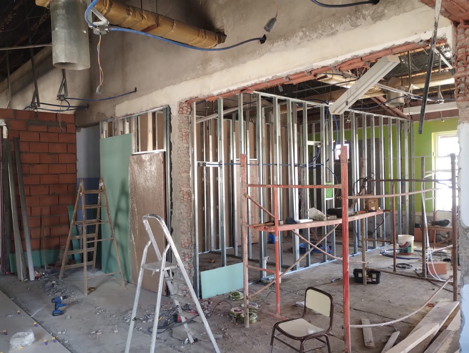 Interior en obras con estructura metálica a la vista, escaleras, andamios y escombros de construcción.