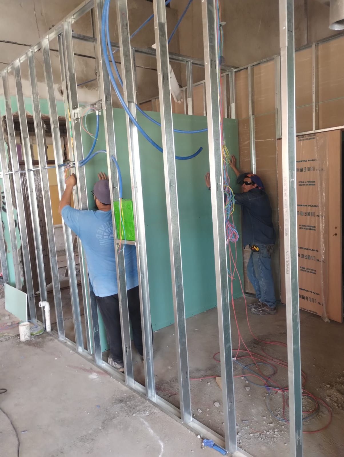 Trabajadores colocando montantes metálicos en las paredes interiores de una obra en construcción.
