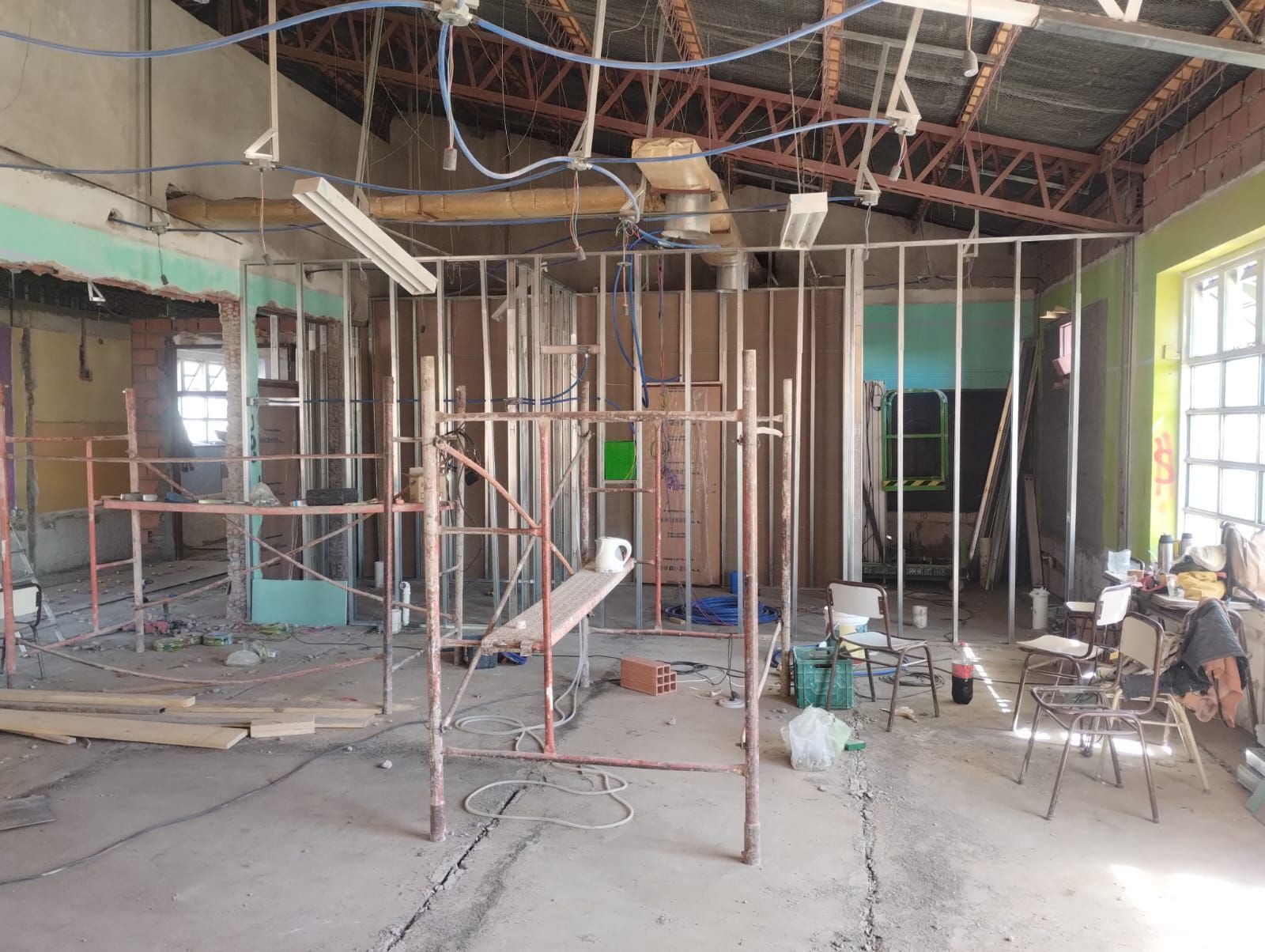Interior en obras de renovación con andamios metálicos, cableado del techo a la vista y herramientas esparcidas por el suelo.