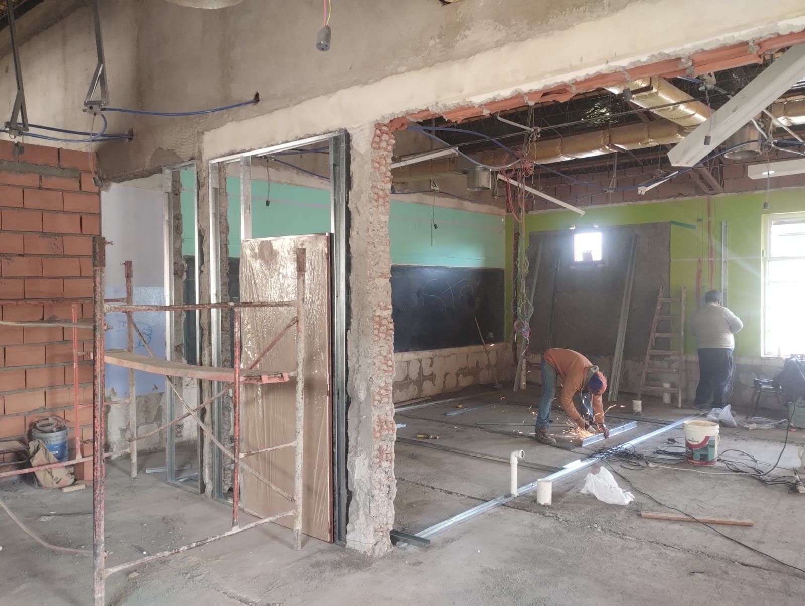 Interior parcialmente demolido con trabajadores, vigas expuestas, andamios y escombros de construcción.