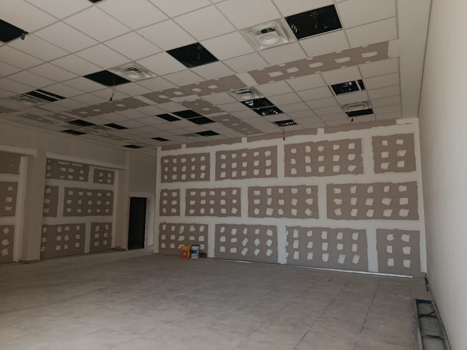 Habitación sin terminar con parches de paneles de yeso, placas de techo suspendido y un piso de concreto en construcción.