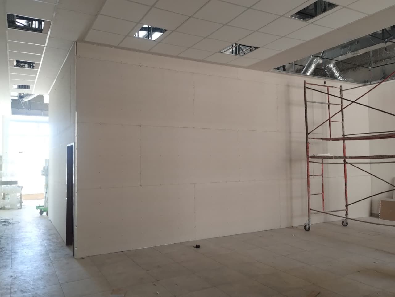 Área de construcción vacía con paredes blancas, piso de concreto y andamios metálicos cerca de la pared derecha.