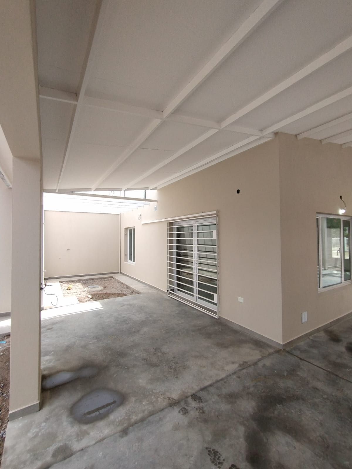 Patio cubierto de hormigón junto a una casa de color beige con vigas 