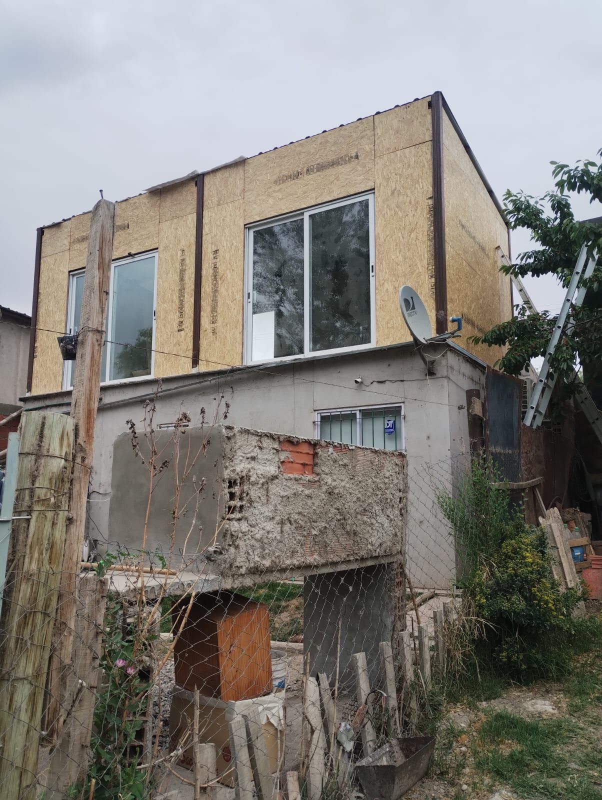 Casa ruinosa de dos plantas con estuco desconchado, ladrillos a la vista y vegetación descontrolada a su alrededor.