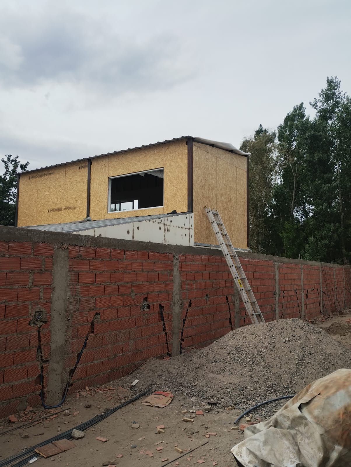 Muro de ladrillo parcialmente construido y edificio amarillo en construcción, con una escalera apoyada contra él.