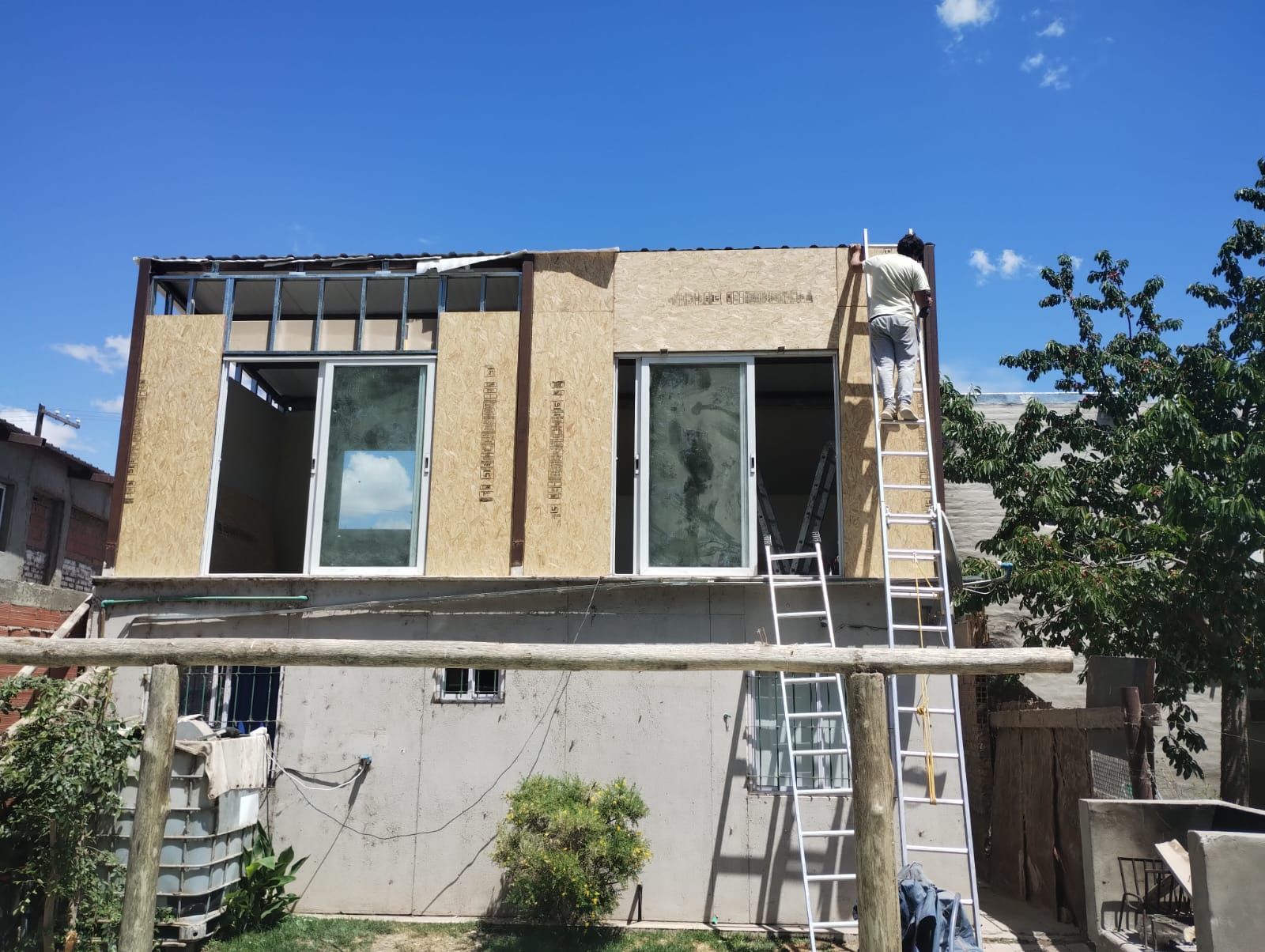 Casa de dos plantas en obras de renovación con escaleras, andamios y paredes exteriores sin terminar.