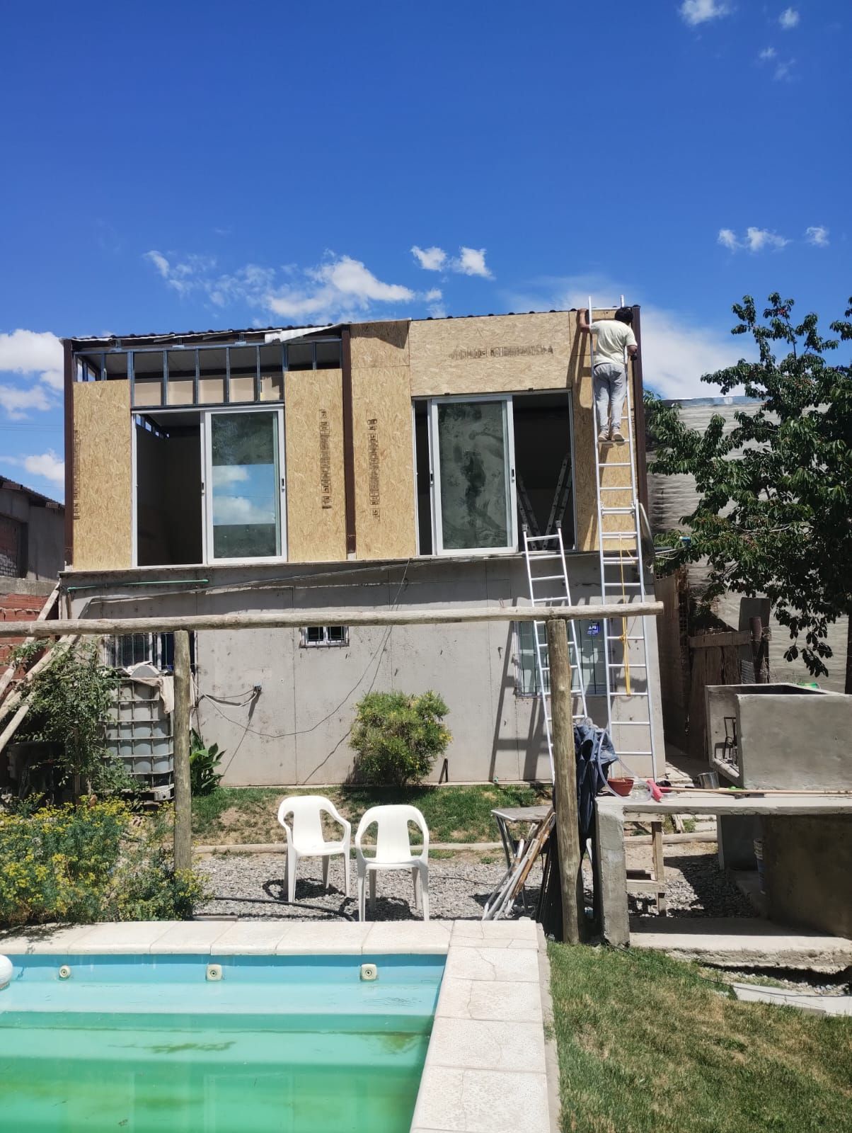 Patio trasero con una pequeña piscina y una casa de dos pisos en construcción, cielo azul sobre nuestras cabezas.