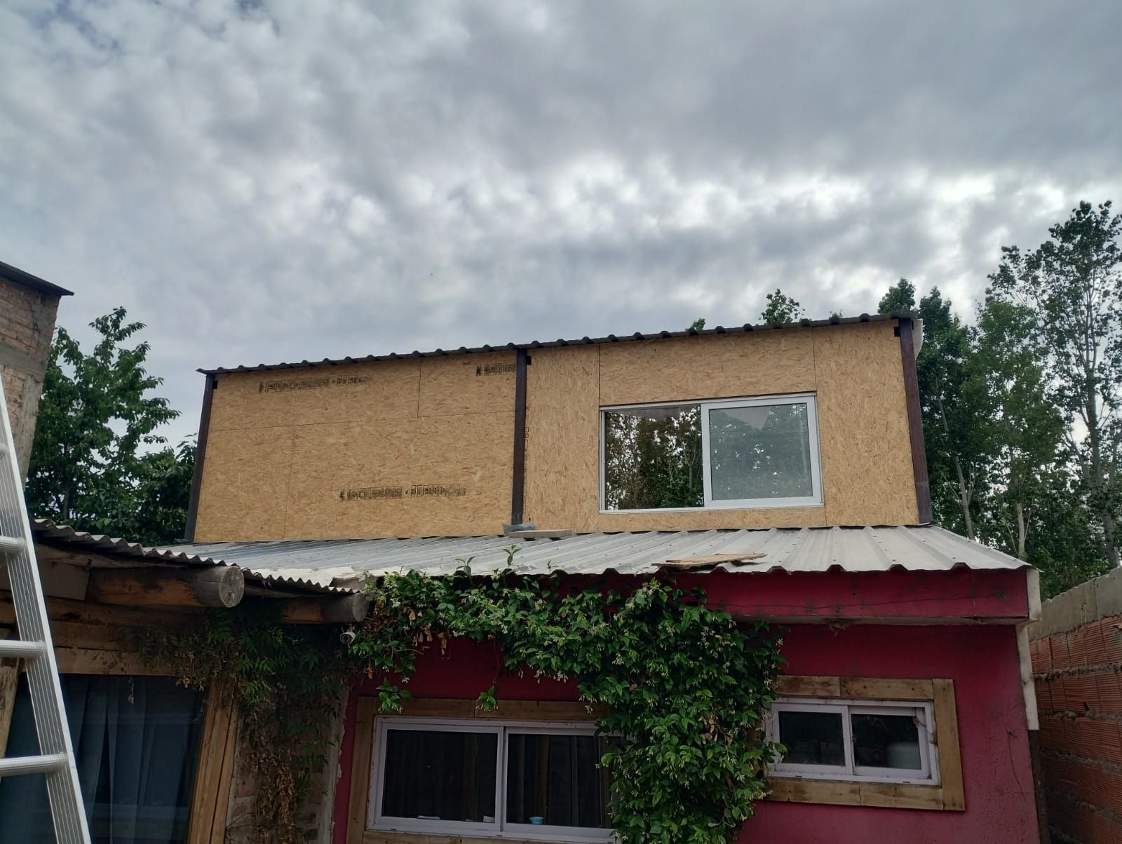 Pequeña casa de dos plantas con la planta baja roja y las paredes superiores de color beige bajo un cielo nublado.