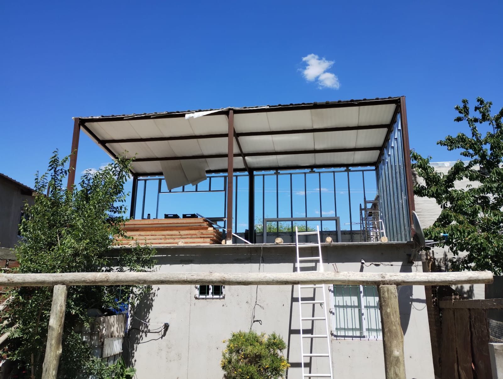Estructura en la azotea parcialmente construida con armazón metálico, una escalera y cielo azul.