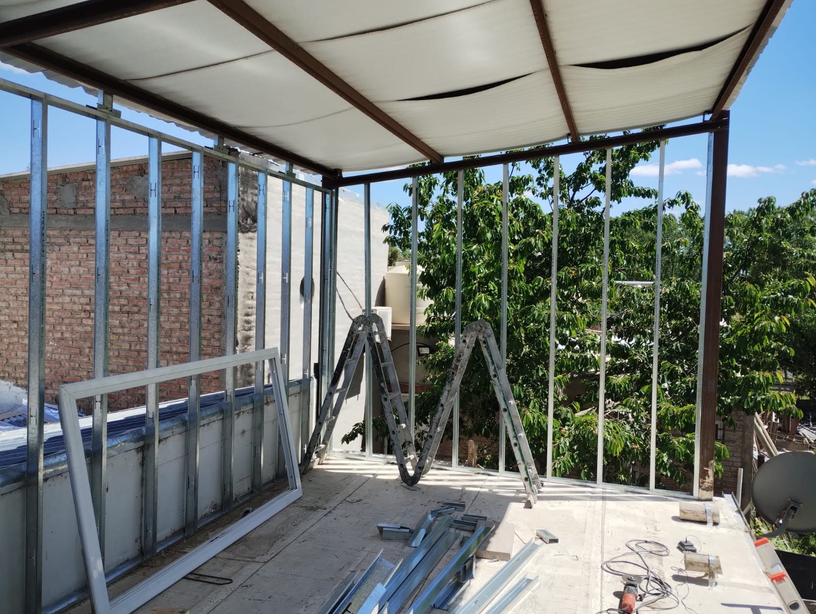 Terraza en construcción en la azotea con barandillas metálicas, estructura del techo y herramientas en el suelo.