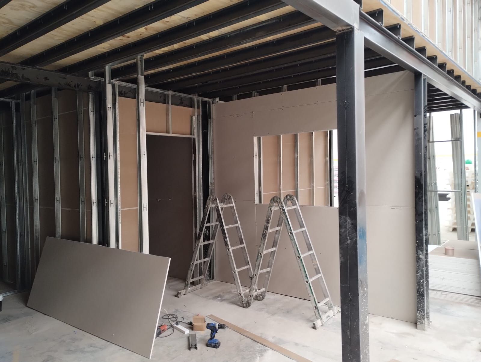 Reforma interior con estructura metálica, paneles de pladur y dos escaleras en una habitación parcialmente terminada.