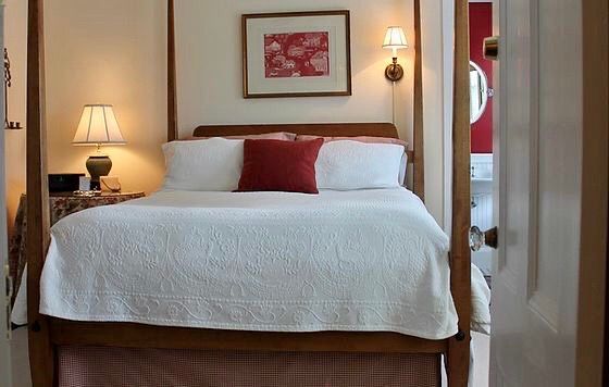 A bedroom with a four poster bed and a picture on the wall above it