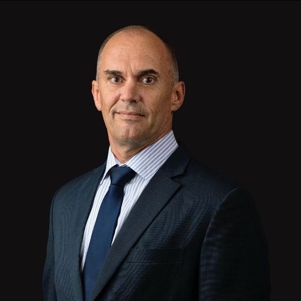 A headshot of a professional wearing a dark suit, blue tie, and light pinstriped shirt against a black background.