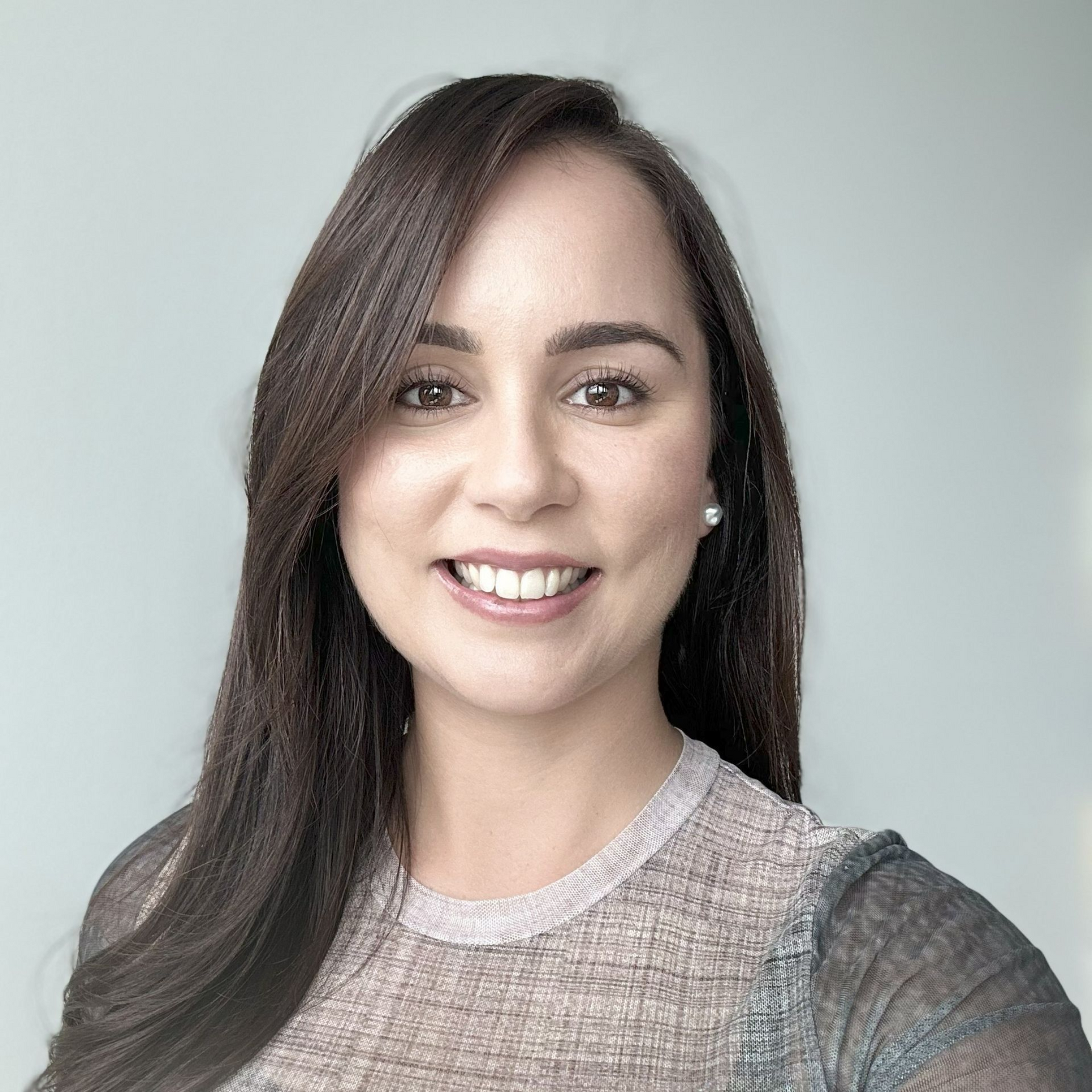 A person with long, dark hair smiling at the camera, wearing a textured, dark gray top against a light, neutral background.