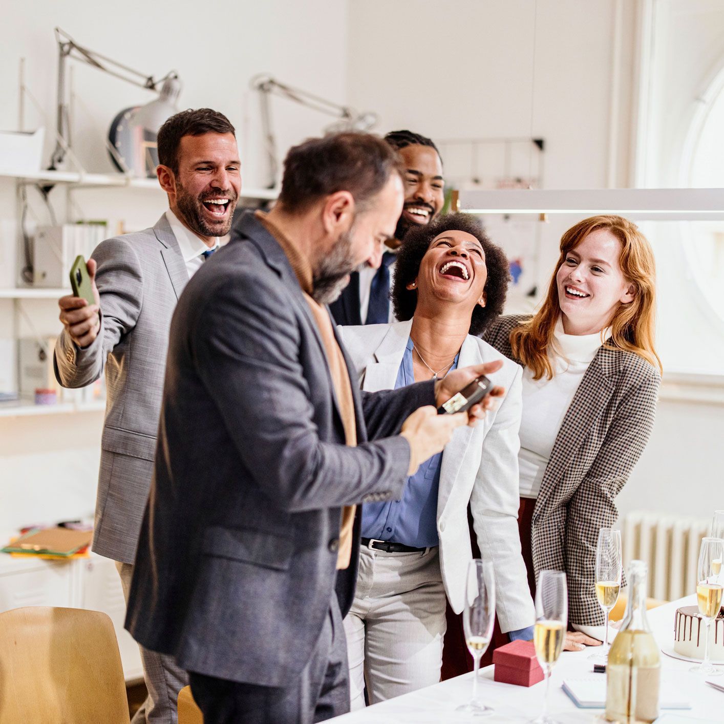 a group of people are standing around a table laughing .