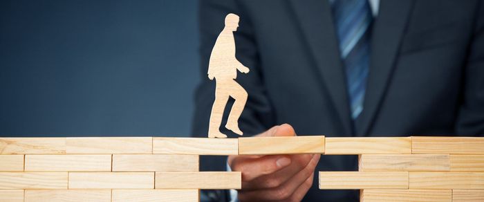 a man in a suit is holding a wooden figure of a man walking across a wooden bridge