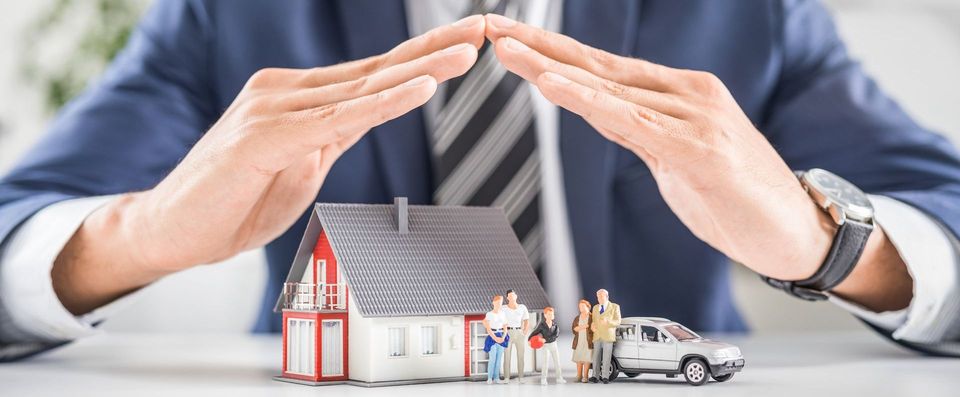 a man in a suit and tie is covering a model house with his hands .