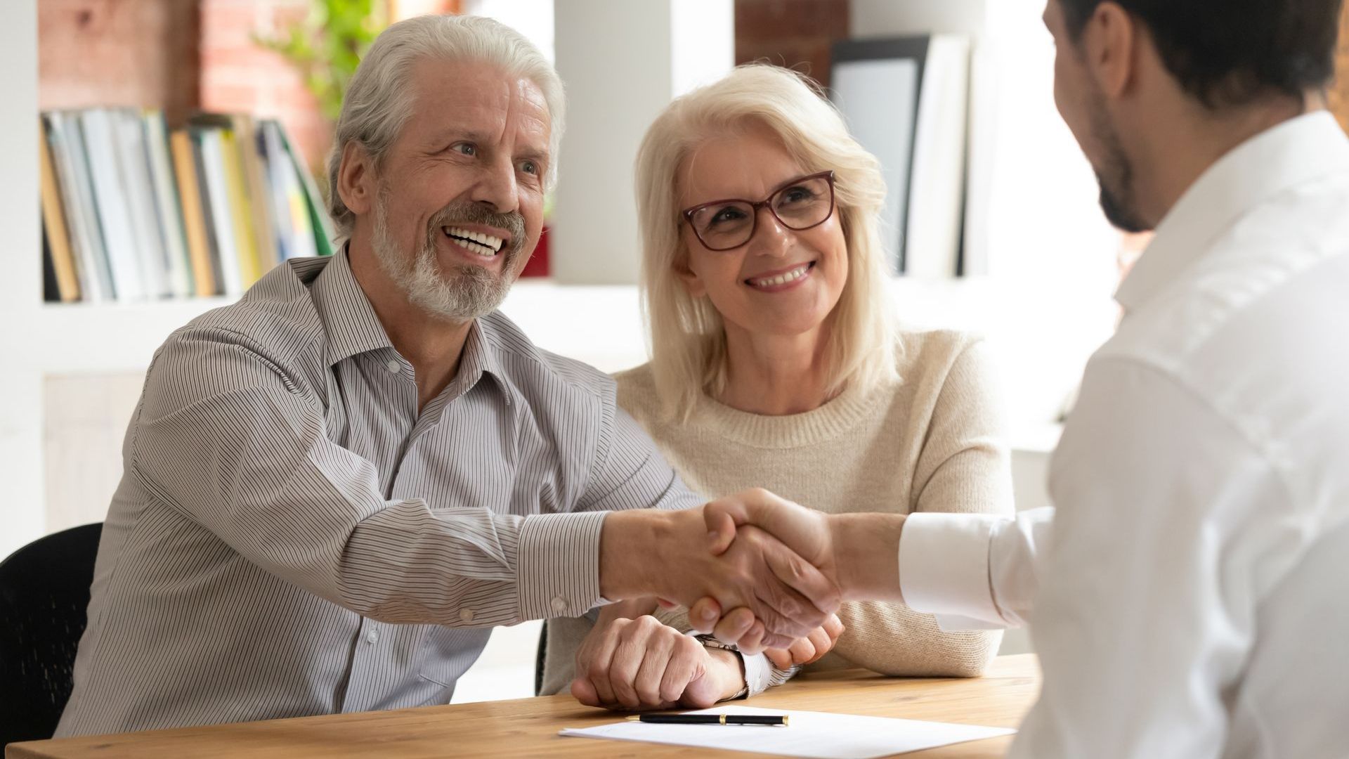 an older couple is shaking hands with a man at a table .