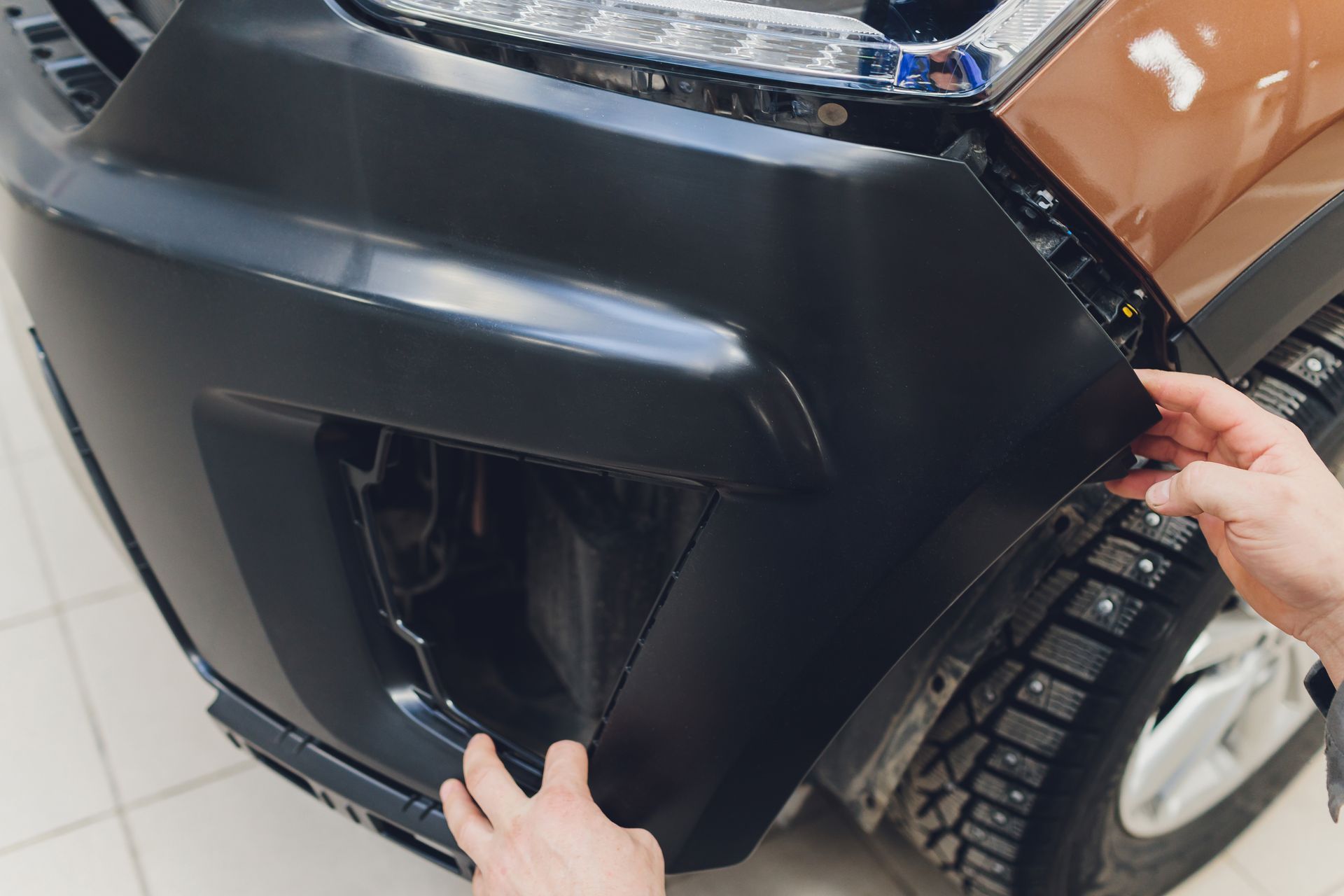 Person installing a black car bumper on a brown vehicle.