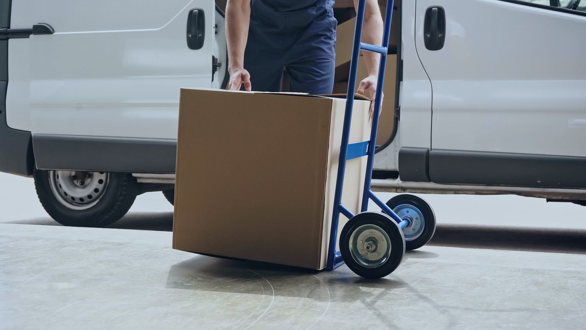 Person loading cardboard box onto a dolly next to a white van.