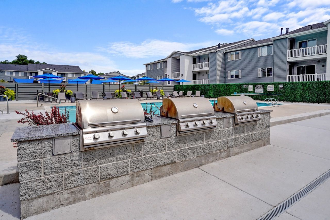 Outdoor community grill station with three built-in grills beside a pool.  Come tour Turnberry Apartments and discover convenient apartments near SLC with easy access to the surrounding area.
