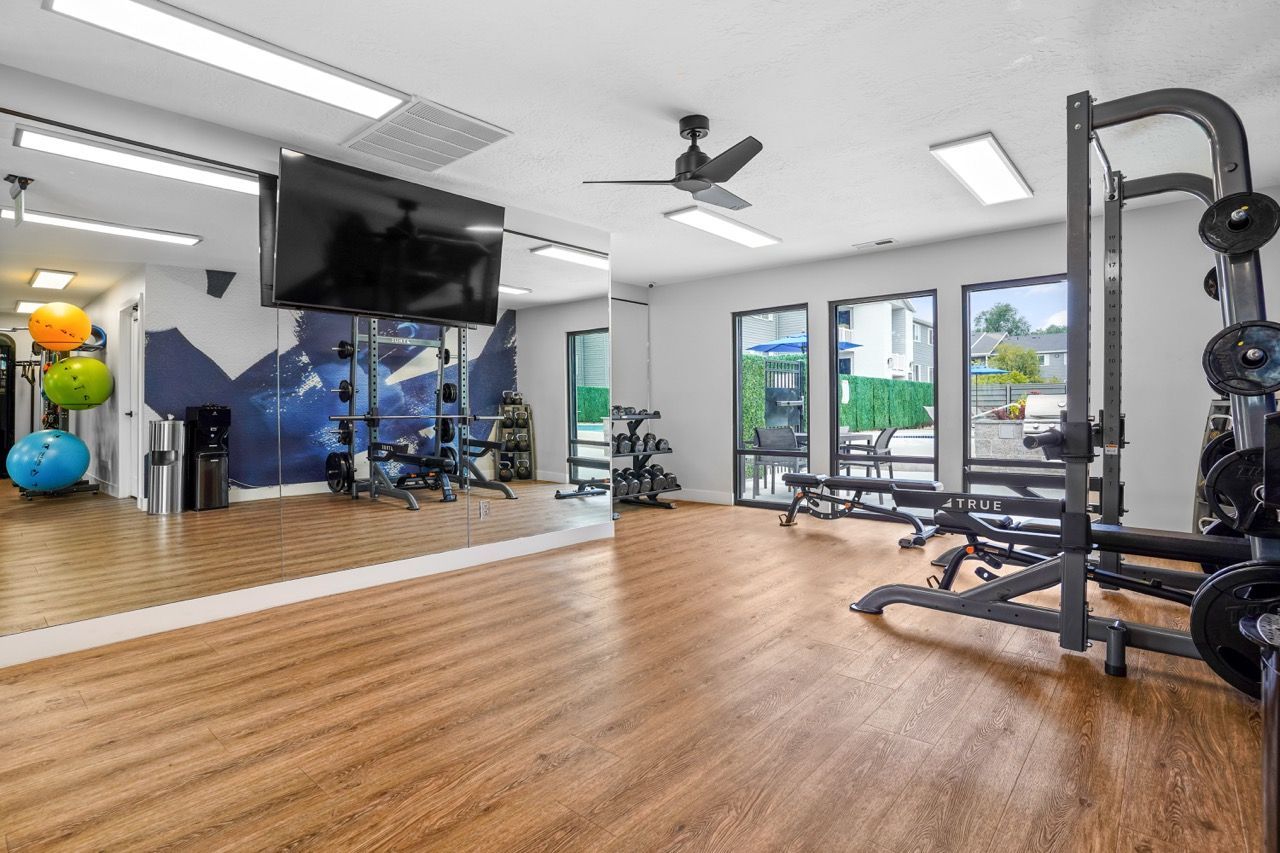 Interior view of a modern resident gym with weights, benches, racks, mirrors, and large windows.  Schedule a walkthrough at Turnberry Apartments and explore renovated apartments for rent in Millcreek, UT designed with modern comfort in mind.
