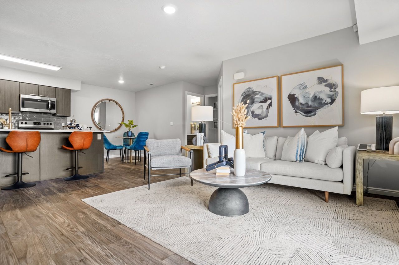 Open-concept living room with a beige sofa, round coffee table, and kitchen island with orange bar stools. Discover convenient apartments near SLC by scheduling a tour at Turnberry Apartments today.
