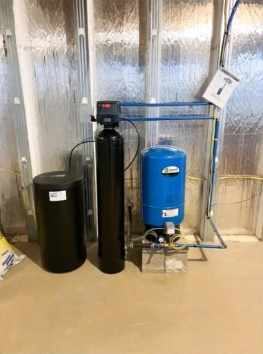 A water filter is sitting next to a blue tank in a basement.