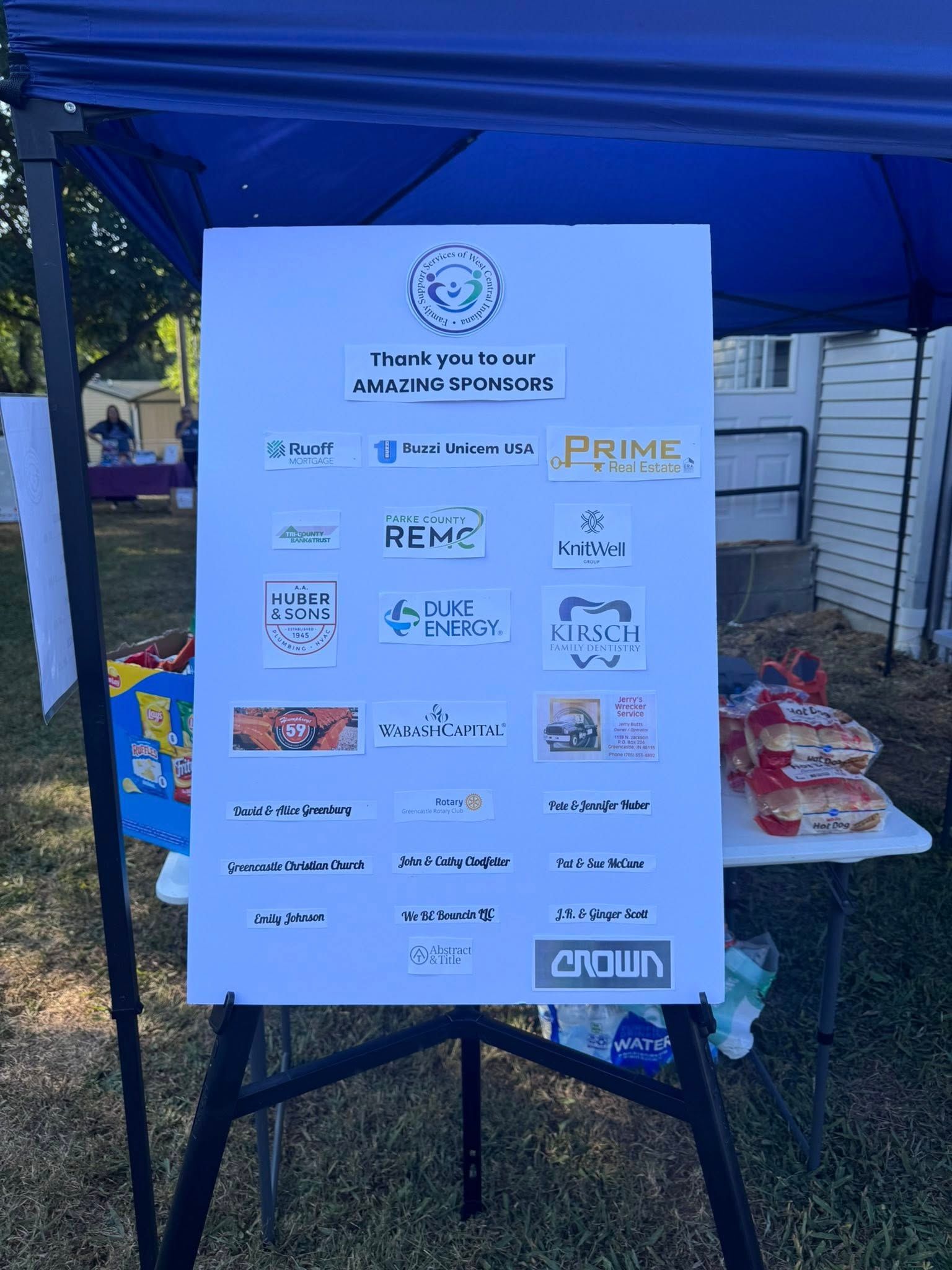 White poster with logos of sponsors, under a blue canopy.