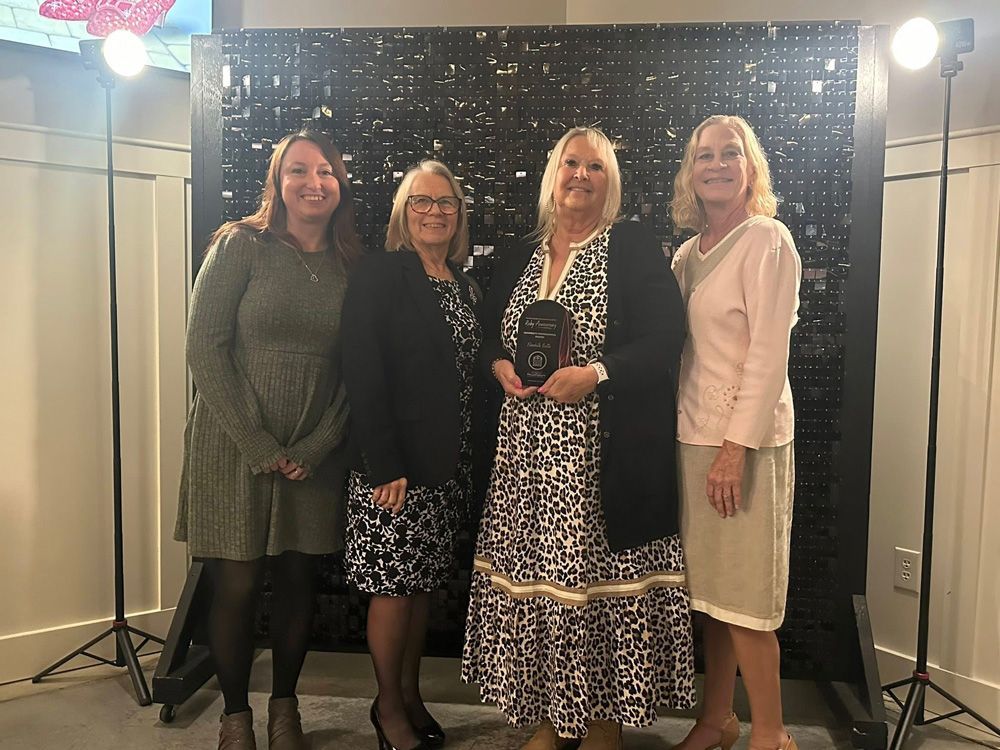 Four women posing with an award in front of a sequined backdrop at an event.
