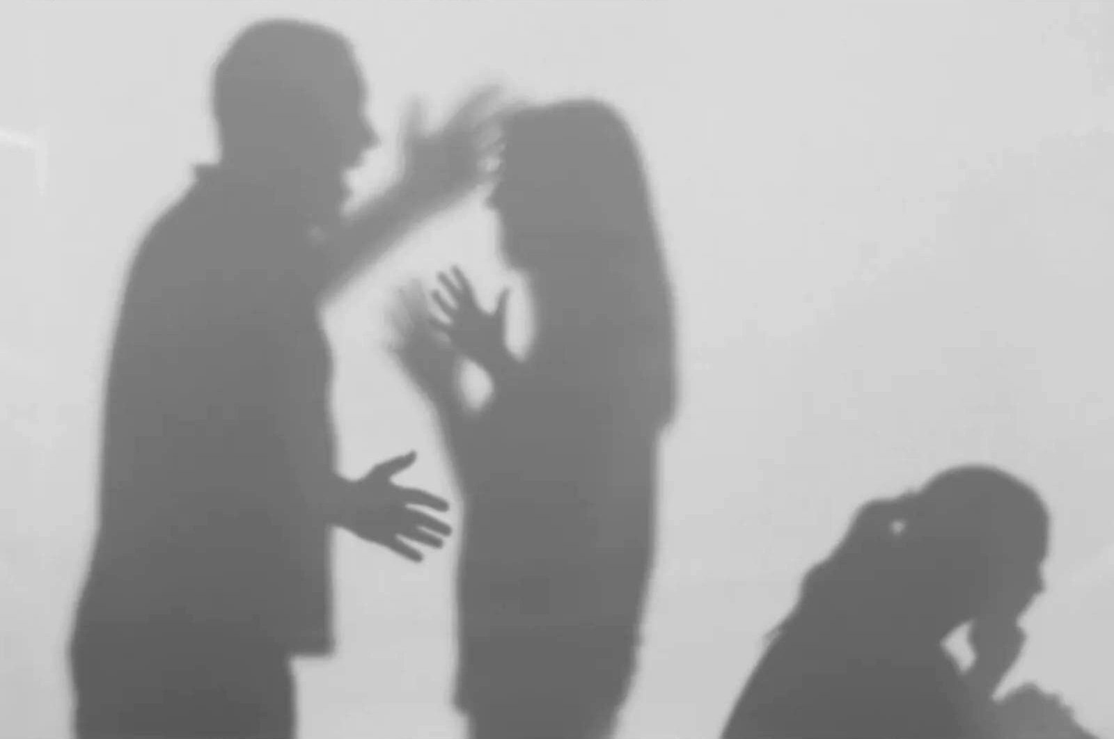 Shadow silhouettes of two people arguing, a third person sits nearby, head in hands.