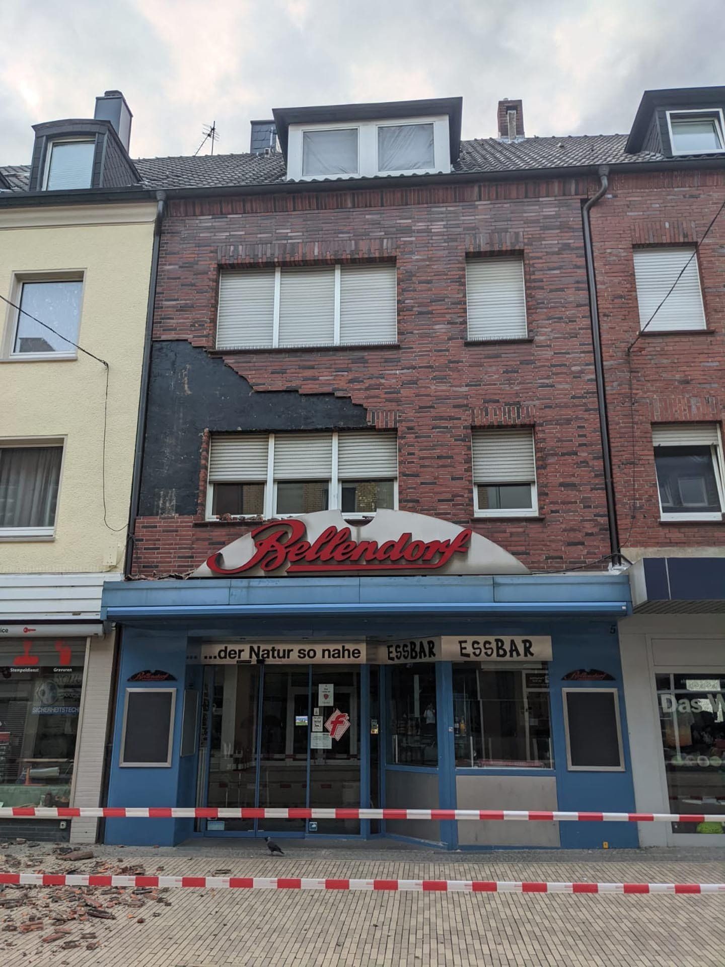 Beschädigtes Backsteingebäude, Schild „Rollendorf“, blaue Fassade mit rot-weißem Absperrband.