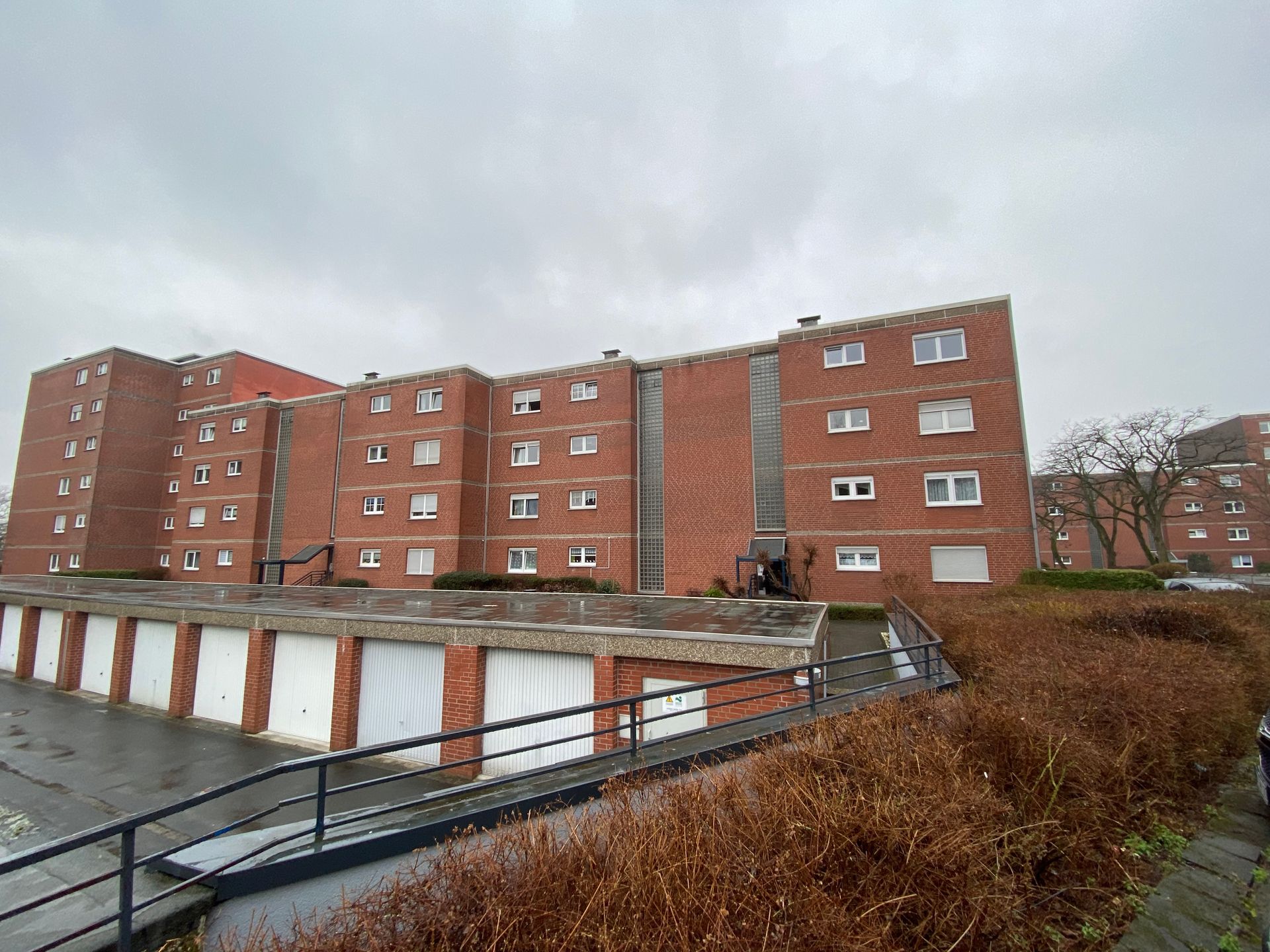 Backstein-Mehrfamilienhaus mit angeschlossenen Garagen und bewölktem Himmel.