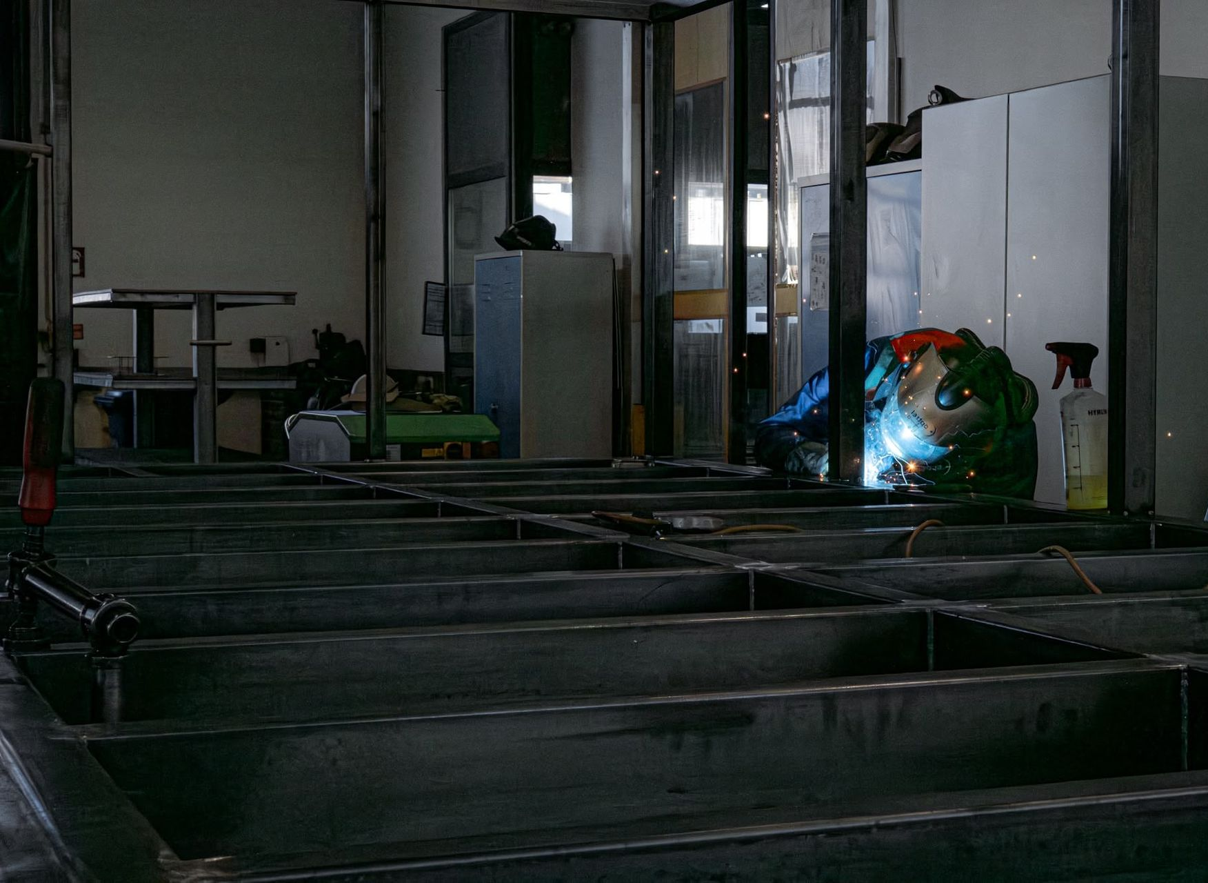 Dunkler Industrieraum mit Metallträgern, Glaspaneelen und einem leuchtend blau-orangen Licht nahe der Rückwand