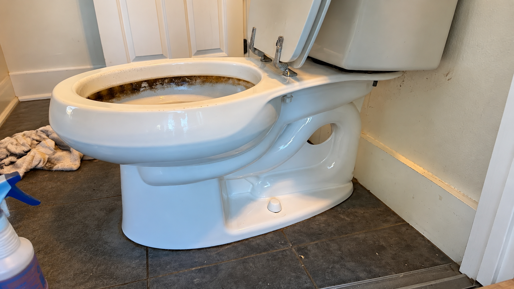 White toilet in a small bathroom, seat raised, with a towel on the floor nearby.